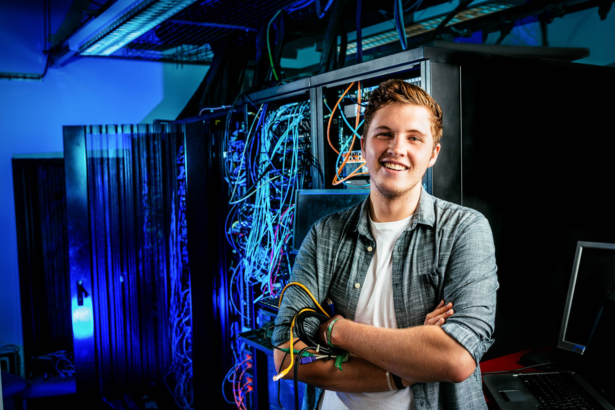 A photo of an IT student holding cables in front of a large networking cabinet