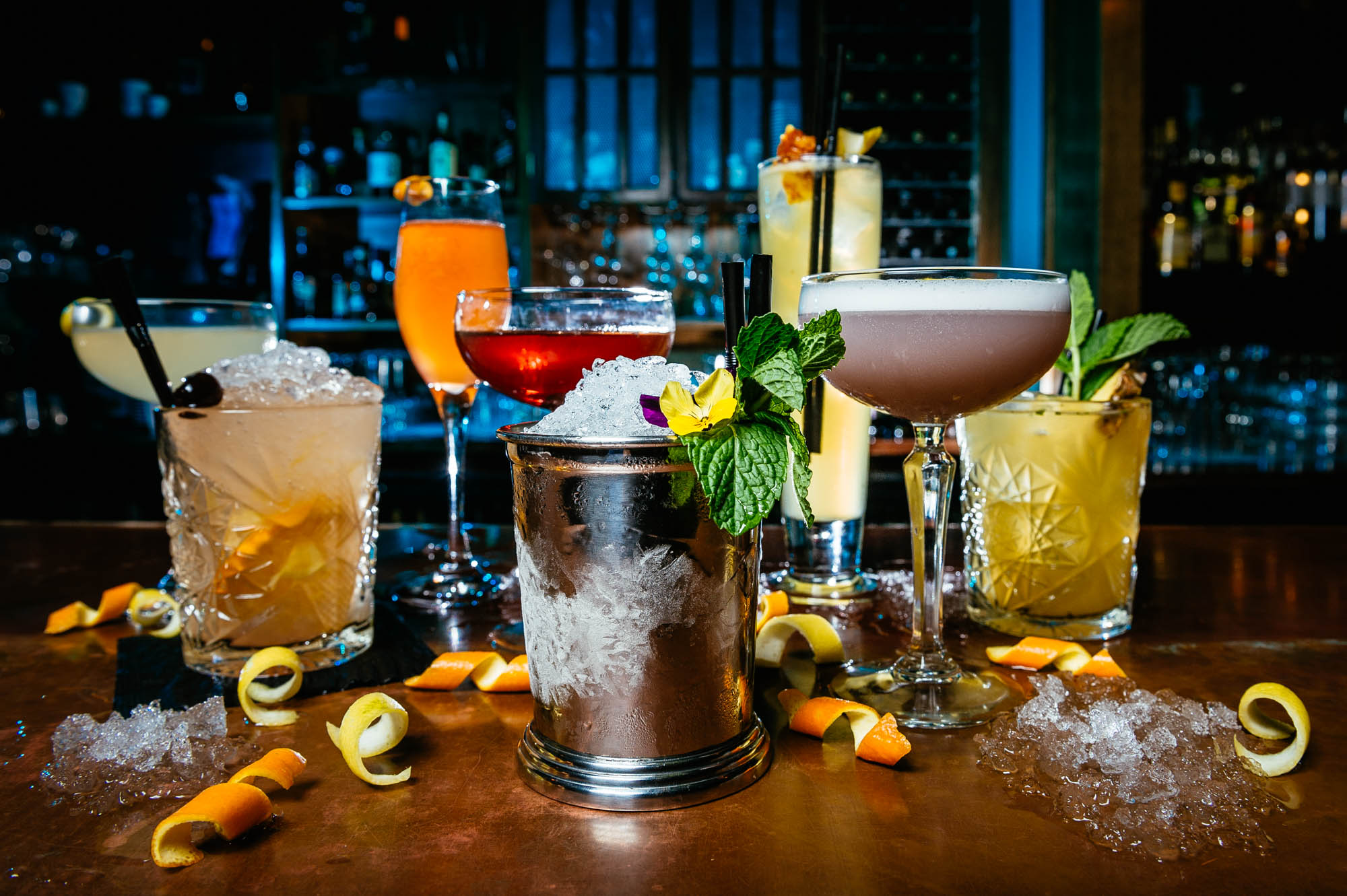 A photo of a set of seven different cocktails on a bar
